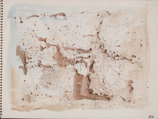 An abstract watercolor of sepia-toned splatters on a page of a bound sketchbook.