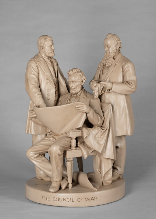 A sculpture of Abraham Lincoln, seated, reading a paper between two standing men.