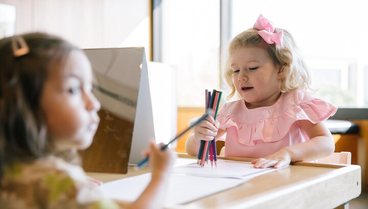 Two toddlers draw on paper with colored pencils.
