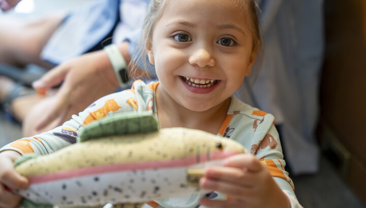 A close-up of a smiling child who is holding up a toy to see.