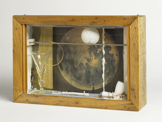 A wood shadowbox containing a pipe, a white ball with gray speckles, a picture of the moon, and a glass goblet.