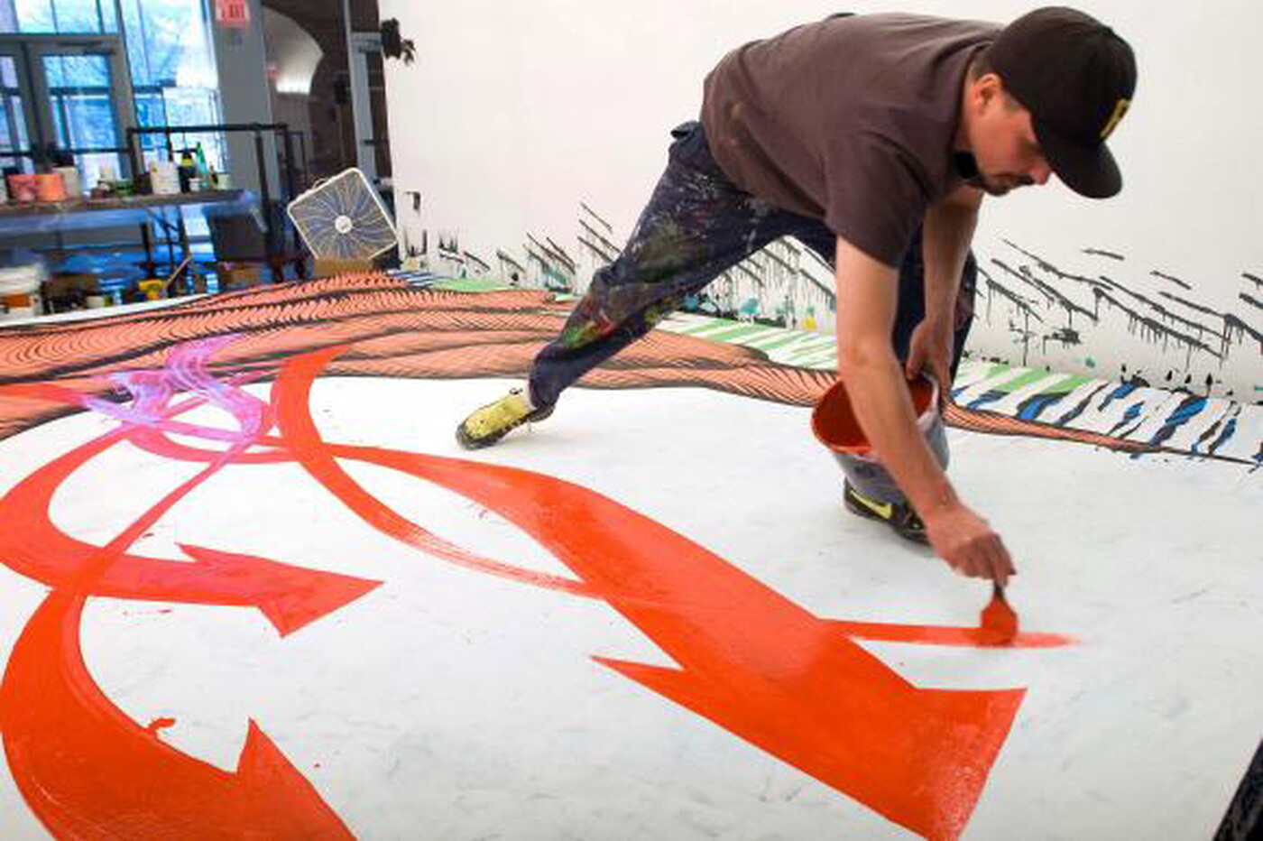 A White man bends over to paint orange shapes onto a mural.