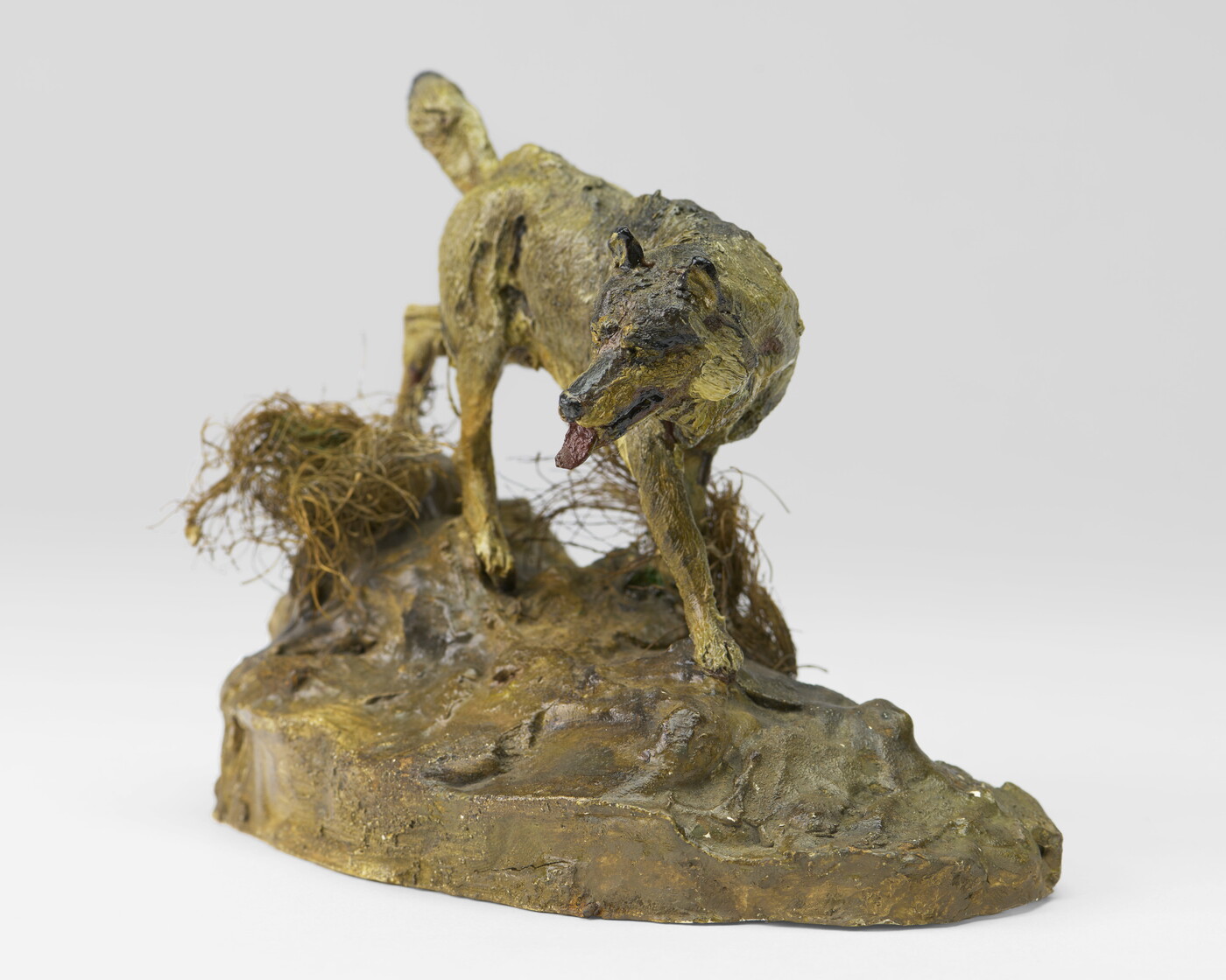 A painted sculpture of a wolf walking across patches of grass on a rock.