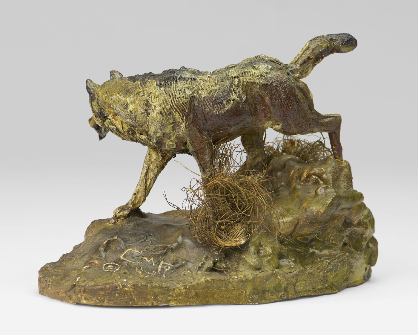A painted sculpture of a wolf walking across patches of grass on a rock.