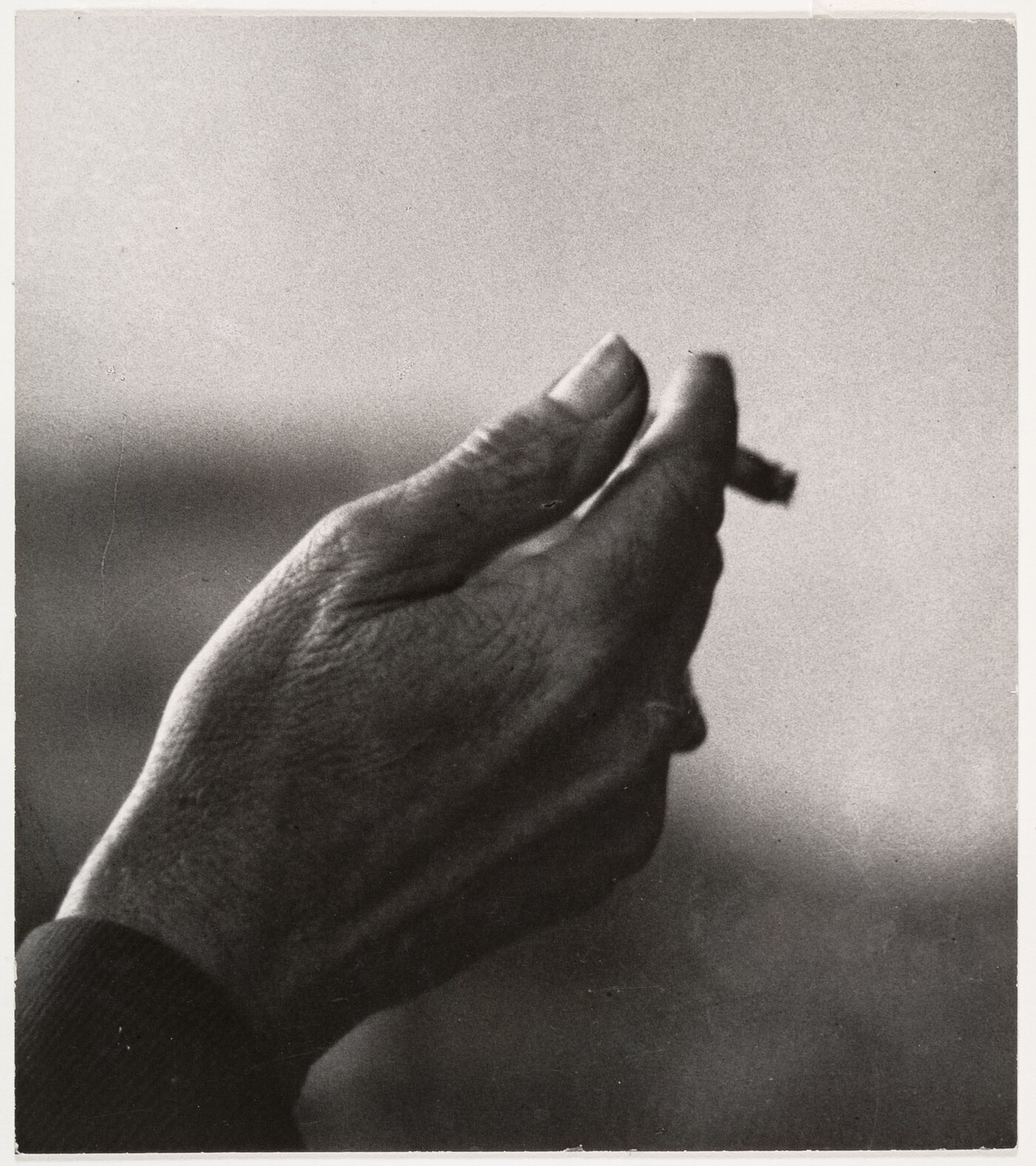 A black-and-white close-up photograph of a right hand holding an almost-finished cigarette.