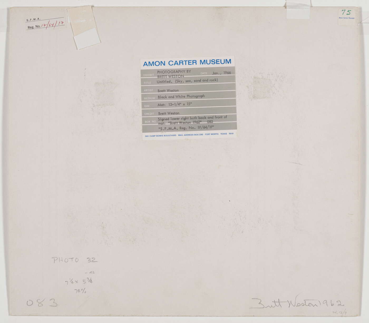 A black-and-white photograph of the sand and sea next to a shore covered with large rocks.