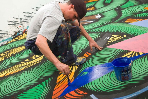 A White man squatting down to apply blue paint to an abstract mural.