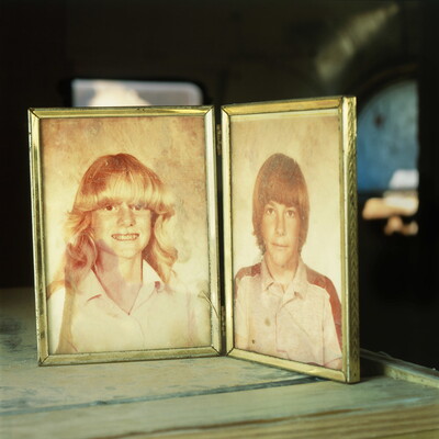 A color photograph of a folding picture frame with faded school photos of of a White girl on the left and a White boy on the right.