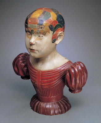 A painted wood sculpture bust of a White child with different parts of the head painted in different colors.