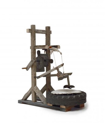 A wood contraption that includes a hand crank that operates a lever with a shoe attached to it that will "stomp" on what looks like a rubber tire.