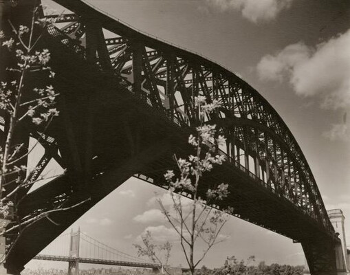 A black-and-white photograph of an arch bridge looking up from beneath one end on a cloudy day.