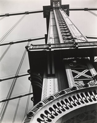 A black-and-white abstract photograph of a partial view of the tower of a suspension bridge from the ground.
