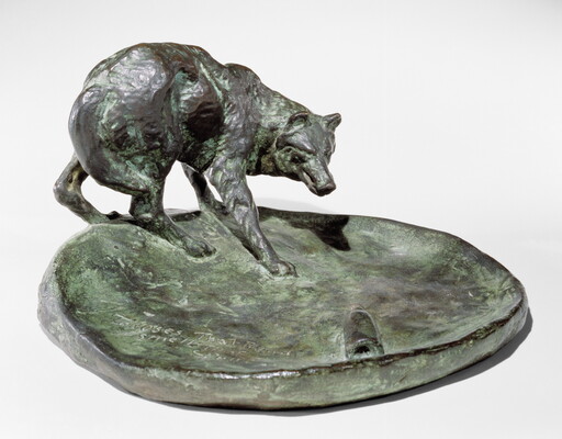 A bronze sculpture of a wolf staring at a bottle on the ground.