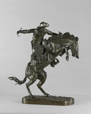 A bronze sculpture of a cowboy balancing on a rearing horse.