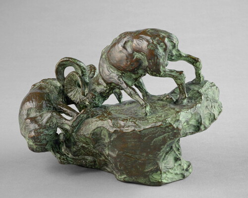 A bronze sculpture of two mountain sheep fighting on the edge of a rock.