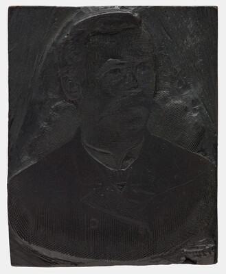 A metal printing block with a portrait of the head and shoulders of a man with a walrus-style mustache, wearing a suit.