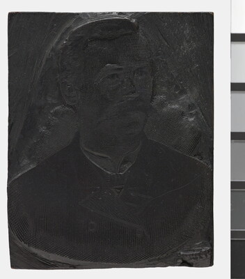 A metal printing block with a portrait of the head and shoulders of a man with a walrus-style mustache, wearing a suit.