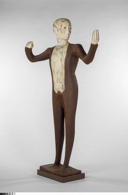 A wood sculpture of a male orchestra conductor standing with his arms raised out to his side.