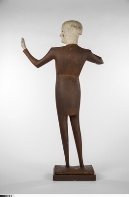 A wood sculpture of a male orchestra conductor standing with his arms raised out to his side.