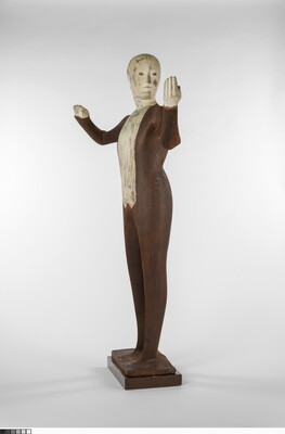 A wood sculpture of a male orchestra conductor standing with his arms raised out to his side.