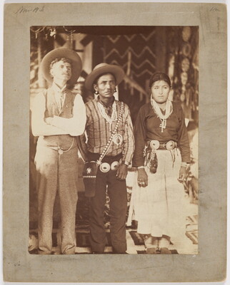 A sepia-toned photograph of three figures [L-R]: a man in western dress, a man wearing a concho belt over western clothing, and a woman in a skirt and blouse with a concho belt.