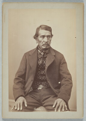 A sepia-toned portrait photograph of a man wearing an open jacket, patterned shirt, and a bowtie.