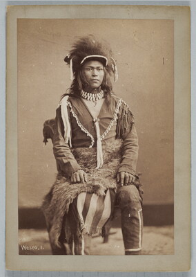 A sepia-toned portrait photograph of a young, Indigenous man seated, wearing traditional dress.