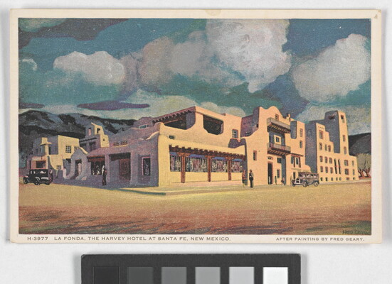 A color postcard of an adobe building with mountains and fluffy white clouds in the background.