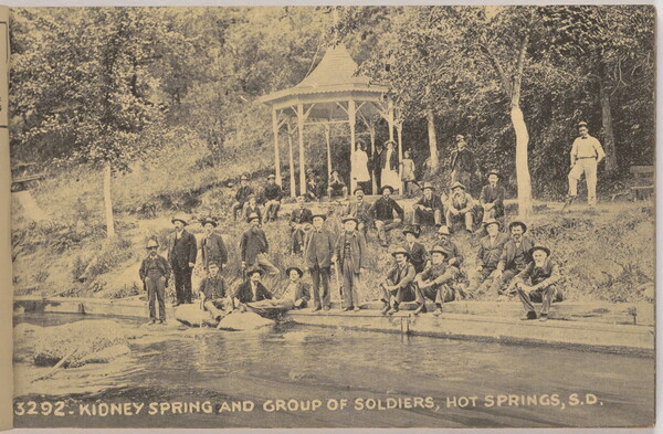 A sepia-toned photograph of a group of men and women seated on a slope and in a gazebo next to a canal.