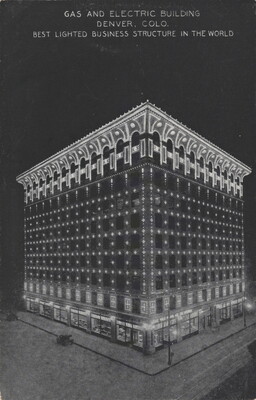 A color postcard of a nine-story building lit up at night under a full moon that is partially hidden behind clouds.