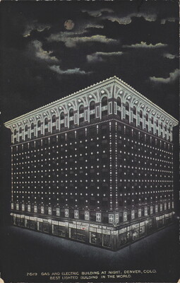 A color postcard of a nine-story building lit up at night under a full moon that is partially hidden behind clouds.
