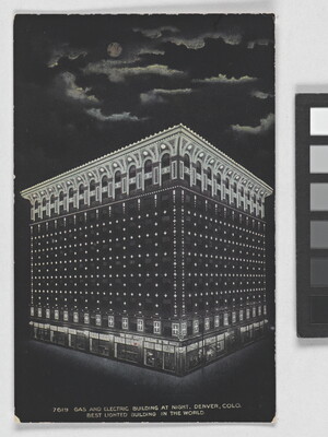 A color postcard of a nine-story building lit up at night under a full moon that is partially hidden behind clouds.