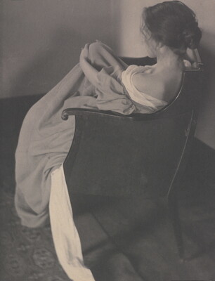A black-and-white photograph of the back of a seated White woman wearing a long off-the-shoulder dress with her hair pulled up in a loose bun.