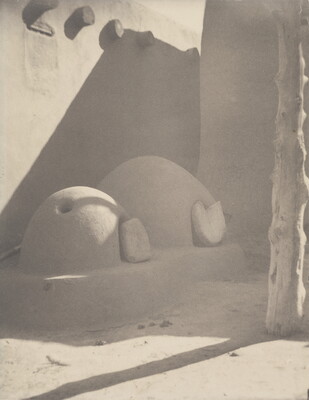 A black-and-white photograph of two beehive ovens attached to an adobe structure.