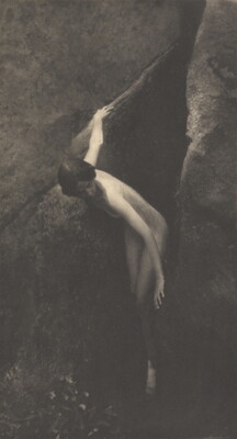 A sepia-toned photograph of a nude White woman emerging from between two large boulders.