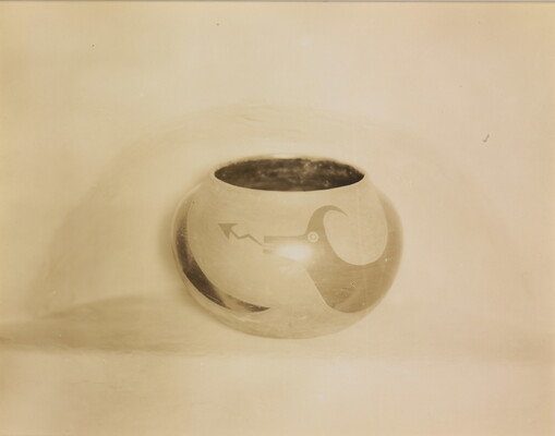 A sepia-toned photograph of a spherical bowl with abstract animal designs on a light background.