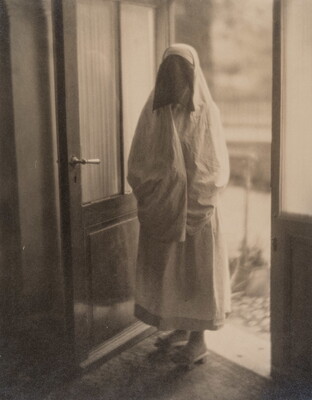 A black-and-white photograph of a woman in a doorway covered from head to toe in a white niqab with dark netting over her face.