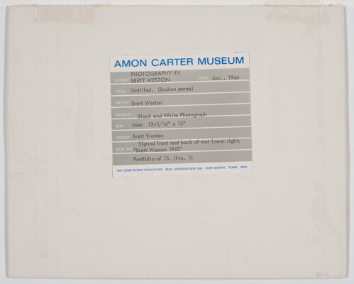 A black-and-white photograph of broken window panes in what looks like a factory building.