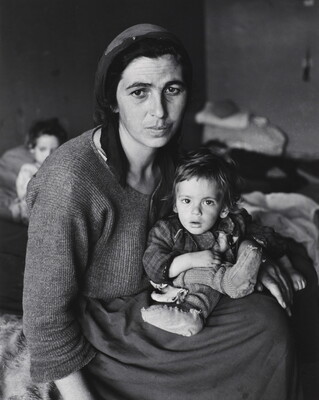 A black-and-white photograph of a tired-looking White woman hunched over a small child in her lap.