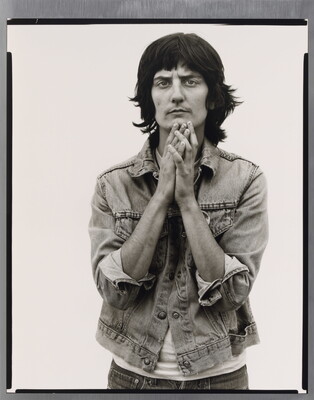 A black-and-white portrait photograph of a light-skinned woman wearing a denim jacket and holding her hands together up to her chin.