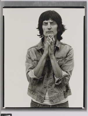 A black-and-white portrait photograph of a light-skinned woman wearing a denim jacket and holding her hands together up to her chin.