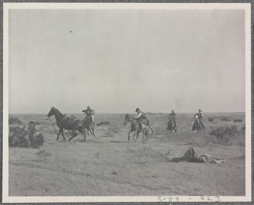 A black-and-white photograph of a group of men on horseback and one man lying on the ground.
