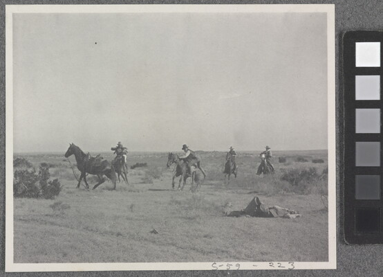A black-and-white photograph of a group of men on horseback and one man laying on the ground.