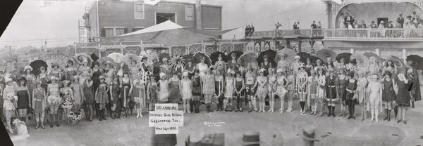 A black-and-white panoramic photograph of a large group of women in different 1920s-style bathing suits, some with parasols.