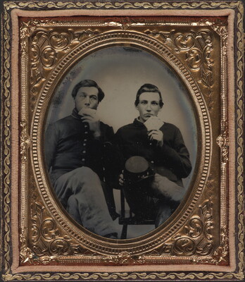 A black-and-white photograph in a decorative copper frame of two seated White men in military uniforms eating large crackers.