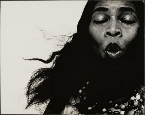 A black-and-white close-up photograph of a Black woman singing with her eyes closed.