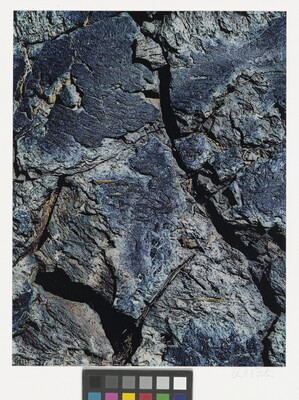 A color close-up photograph of a rough blue-tinged rock with cracks.