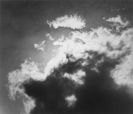 A black-and-white photograph of dappled dark clouds in front of the bright sun.
