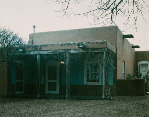 A color photograph of an adobe building with a wooden porch.