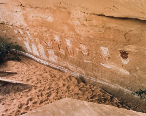 A color photograph of the base of a rock wall with petroglyphs on it.